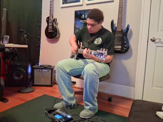 Guitarist tracking a part in a home studio, guitars hanging on the wall
