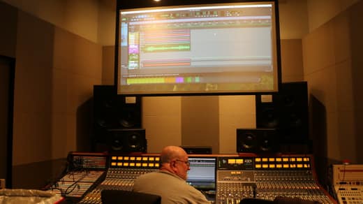 Engineer at a large analog mixing console beneath a projection of the session