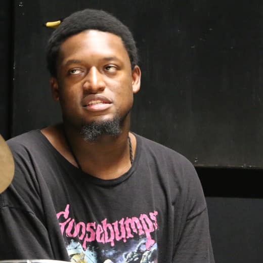 Jeffrey Huff seated between two cymbals against a black wall